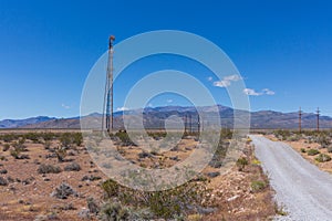 An empty dirt road among the electricity poles in the middle of the desert landscape and the mountains of Nevada, USA