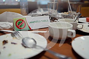 Empty dishes on the dining table with sanitized table sign in a restaurant, COVID-19 pandemic, coronavirus spread preventive