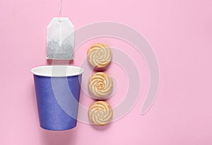 Empty disposable paper cup for tea, tea bag, cookies on pink pastel background, top view, minimalism.