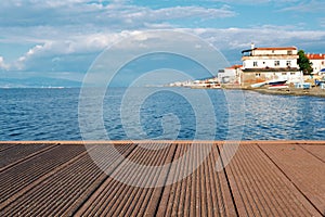 Empty dock or pier platform with brown waterproof decking with sea, sky and house background