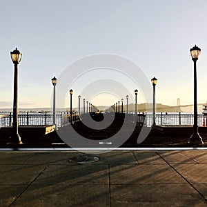 Empty dock with street lamps leading to the sea at sunset