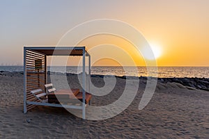 Empty double sun bed with pillows on the sandy beach in Dubai, with orange sunset in the background and calm sea