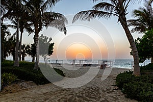 Empty double sun beds on the sandy beach in Dubai, with orange sunset in the background and calm sea