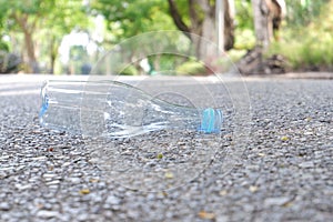 An empty of drinking plastic bottle littering on the ground floor in plubic park road with blurred street  background