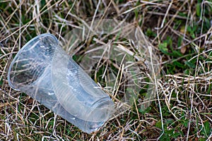 Empty, dropped  plastic cup in lifeless vegetation at early spring