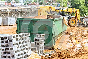 An empty dumpster for construction waste debris near a construction site is loaded up with debris