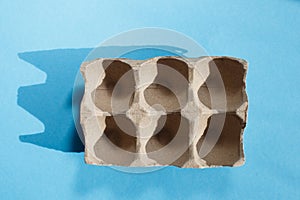 Empty eggs carton box with hard shadows on blue background.