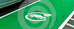 Empty electric vehicle charge station parking spot, marked green zone, car charging device symbol on the asphalt, nobody. Eco