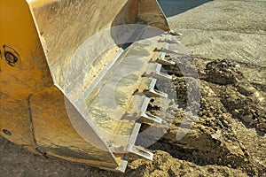 An empty excavator bucket with numerous scratches and paint chips, over a buried trench. Concept of construction, repair