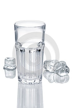 Empty faceted glass and three ice cubes melting on white glass table