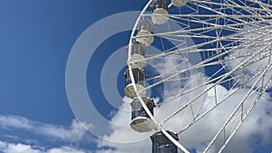 Empty Ferris wheel rotating against blue sky with white clouds