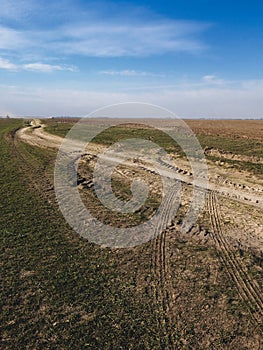 An empty field with a winding dirt road, marked by tire tracks, under clear skies