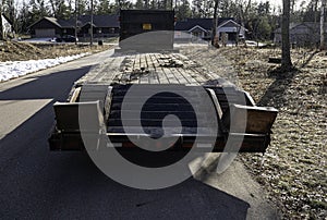 Empty flatbed trailer with raised ramps is parked on the asphalt road