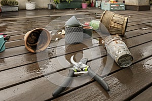 Empty flower pots of all kinds next to assorted gardening objects and various plants on the wooden floor with rusty metal flower