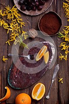 Empty food background with empty plate, oranges, chocolate, yellow flowers, fork and knife on wood board