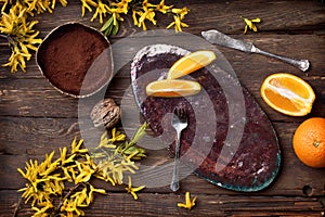 Empty food background with empty plate, oranges, chocolate, yellow flowers, fork and knife on wood board