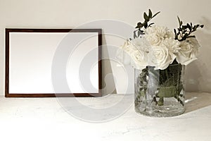 empty frame and bouquet of white roses on a white background with space for text. flowers in a transparent vase with