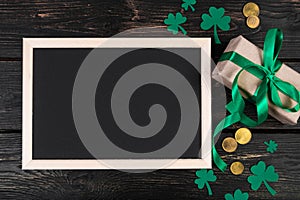 Empty frame for text, gold coins, clover shamrock and gift with green ribbon on a dark wooden background. Good luck