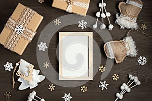 An empty frame on a wooden table surrounded by Christmas gifts and ornaments made of natural materials. A mockup for