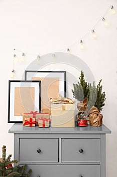 Empty frames, Christmas gifts, evergreen trees and accessories on grey chest of drawers indoors