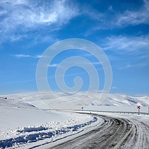 Empty frozen asphalt road and snow covered landscape with mountain over blue sky in winter time