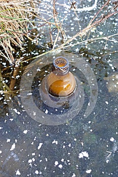 An empty glass bottle was frozen in the ice of the lake. Environmental pollution. Ecology