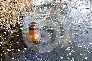 An empty glass bottle was frozen in the ice of the lake. Environmental pollution. Ecology