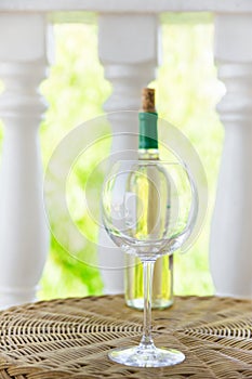 Empty glass bottle with white dry wine on wicker table on garden terrace of villa or mansion. Authentic lifestyle image