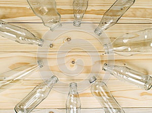 Empty glass bottles lined up in a round manner on light brown background.