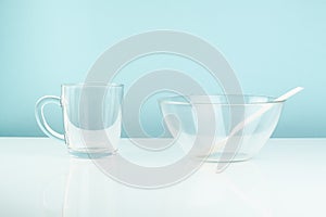 Empty glass bowl and mug on a table. Hunger or diet concept: clean transparrent dinnerware in white and blue background