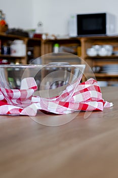 An empty glass bowl stands on a plaid napkin on a wooden table