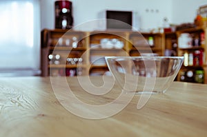 An empty glass bowl stands on a wooden table against a wooden kitchen background