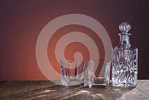 Empty glass carafe, prepared for the alcohol drink on dark orange background and wood