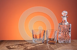 Empty glass carafe, prepared for the alcohol drink on dark orange background and wood