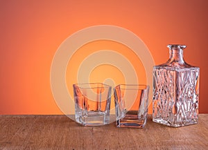 Empty glass carafe, prepared for the alcohol drink on dark orange background and wood