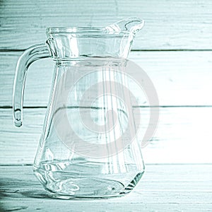 An empty glass carafe for water stands on a white wooden background