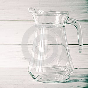 An empty glass carafe for water stands on a white wooden background