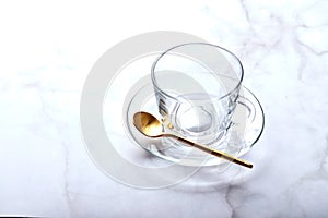 Empty glass cup on saucer with golden spoon on light marble table