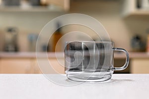 Empty glass cup sitting on laminated kitchen benchtop, Cupboards and cooking appliances in background photo