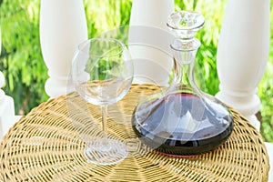 Empty Glass Decanter with Red Wine on Rattan Wicker Table in Garden Terrace of Villa or Mansion. Authentic Lifestyle Image