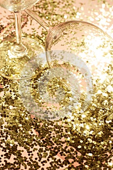 Empty glass goblets for champagne in golden confetti on the table. Festive background. Party concept