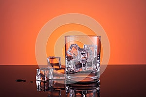 Empty glass with ice prepared for the drink on orange background