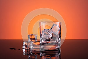 Empty glass with ice prepared for the drink on orange background