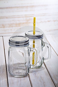 Empty glass mason jar with handle and drinking straw isolated on wood white background