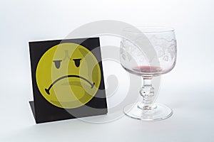 An empty glass of red wine is accompanied by a negative smiley