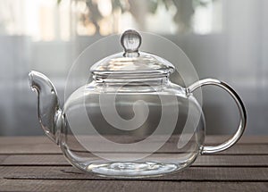 Empty glass teapot on wooden background in front of the window