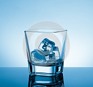 Empty glass of whiskey on black table with reflection and ice on light blue tint background