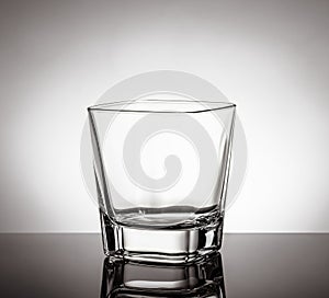 Empty glass of whiskey on black table with reflection on white background