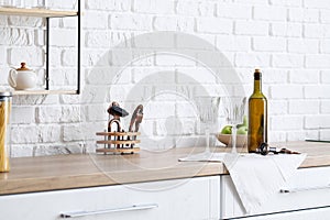 Empty glasses and bottle of wine on kitchen counter near white brick wall