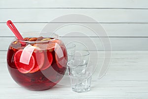 Empty glasses and ladle near bowl of aromatic punch drink on white wooden table, space for text